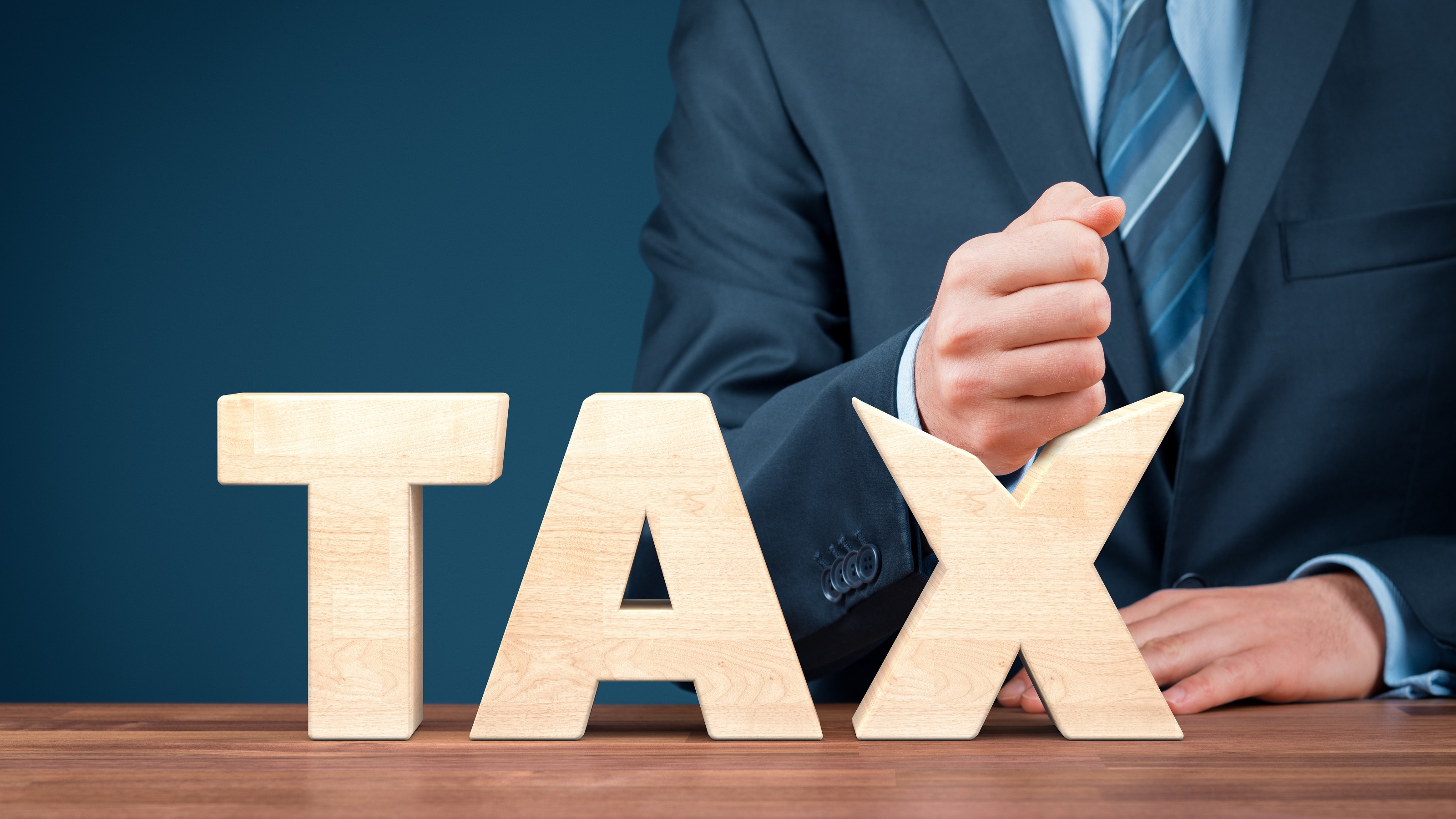 Un homme en costume écrase du poing le X du mot taxe.