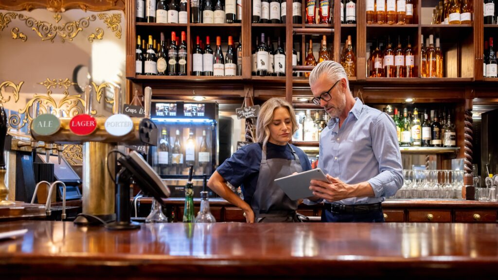 A restaurant business owner talks with an employee behind the bar.