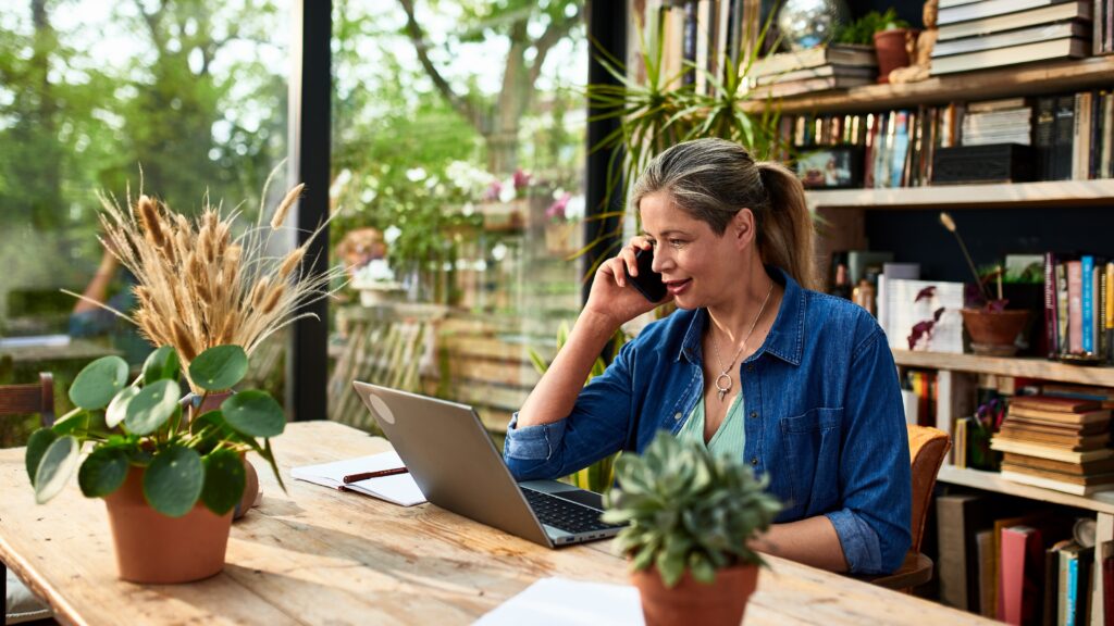 A florist talks on the phone while sitting in front of her laptop in her flower shop.