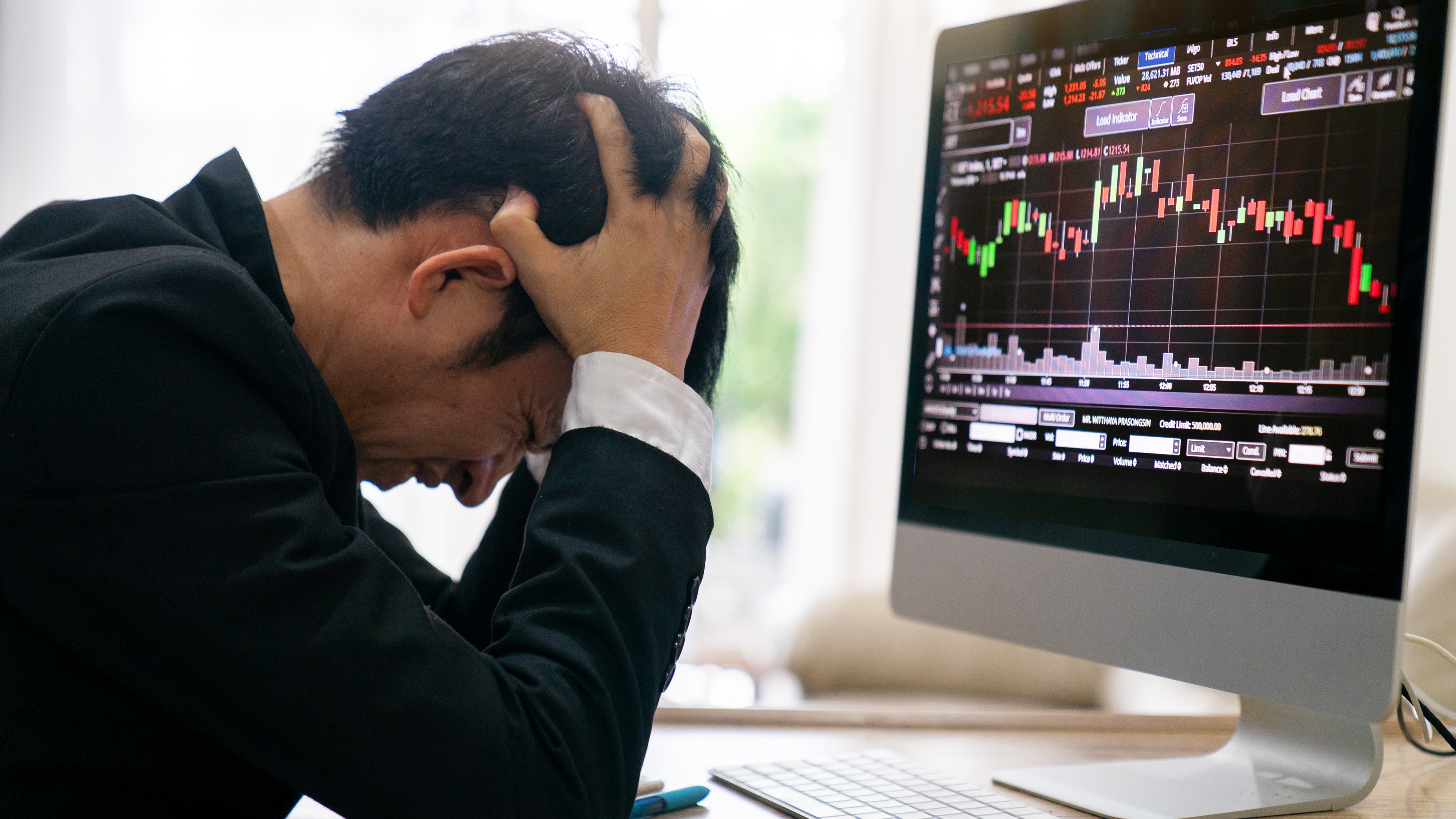 Un investisseur met sa tête entre ses mains devant un graphique de trading sur son ordinateur.