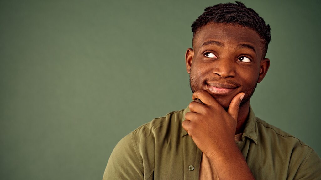 A young man looks into the distance, his hand on his chin as he wonders about something.