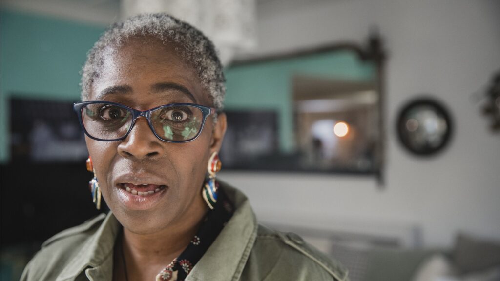 An older woman in her living room looks surprised.