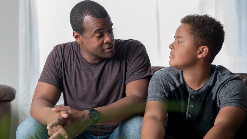 A father has a serious discussion with his son while they sit on the sofa.