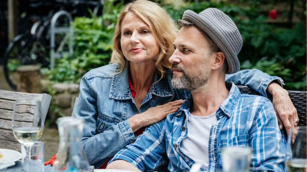 A fiftysomething couple sit very close together while dining outside.