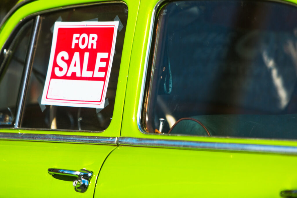 A "for sale" sign is in the window of an old, bright green car.