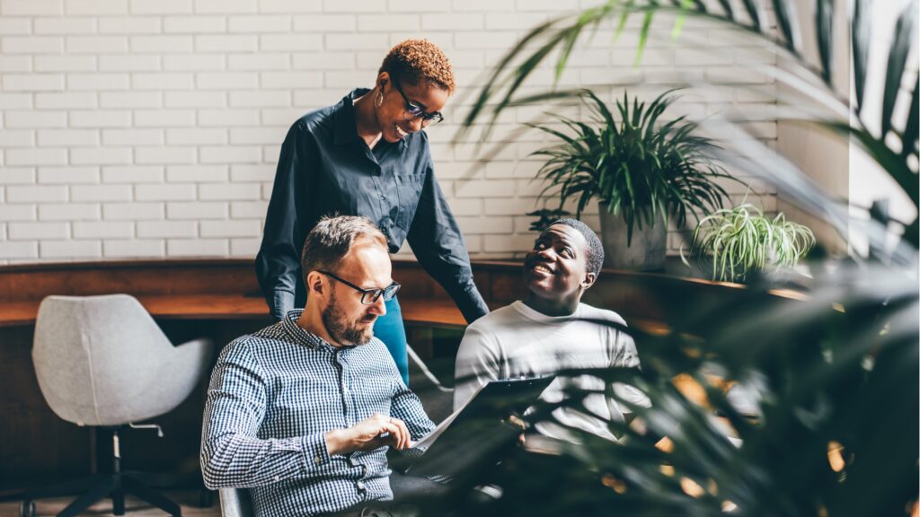 Three employees at a small business interact and smile.