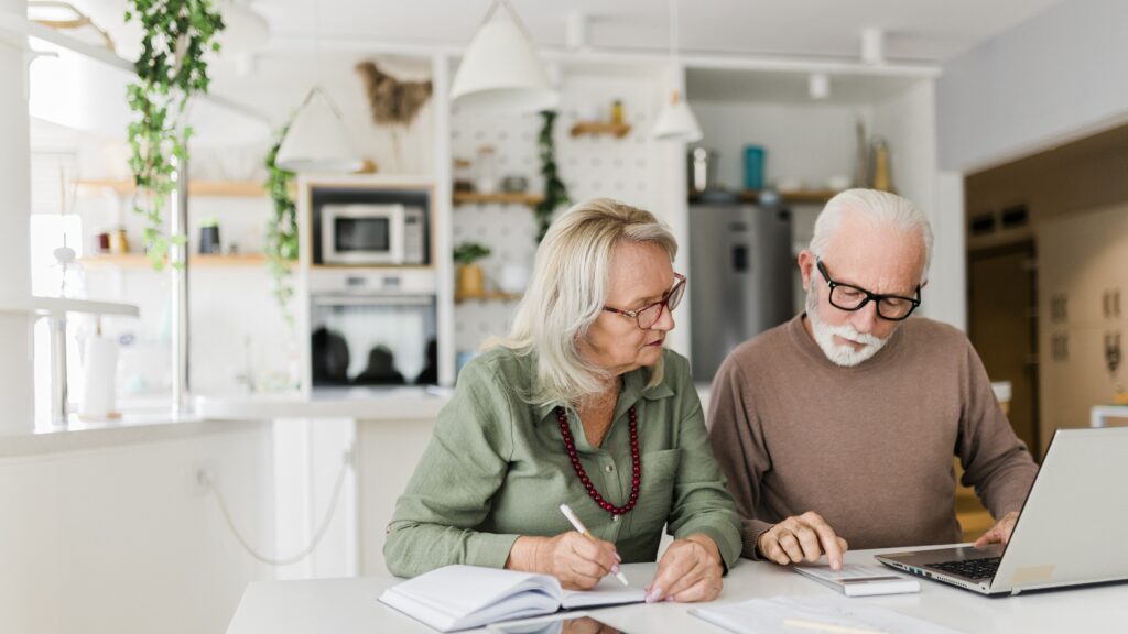 An older couple work together on retirement planning in their kitchen.