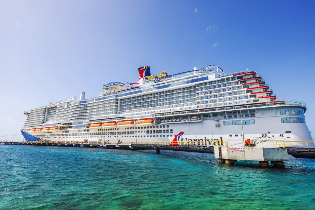 Carnival cruise ship docked in turquoise water Caribbean sea under clear blue sky with lifeboats along white hull near pier.