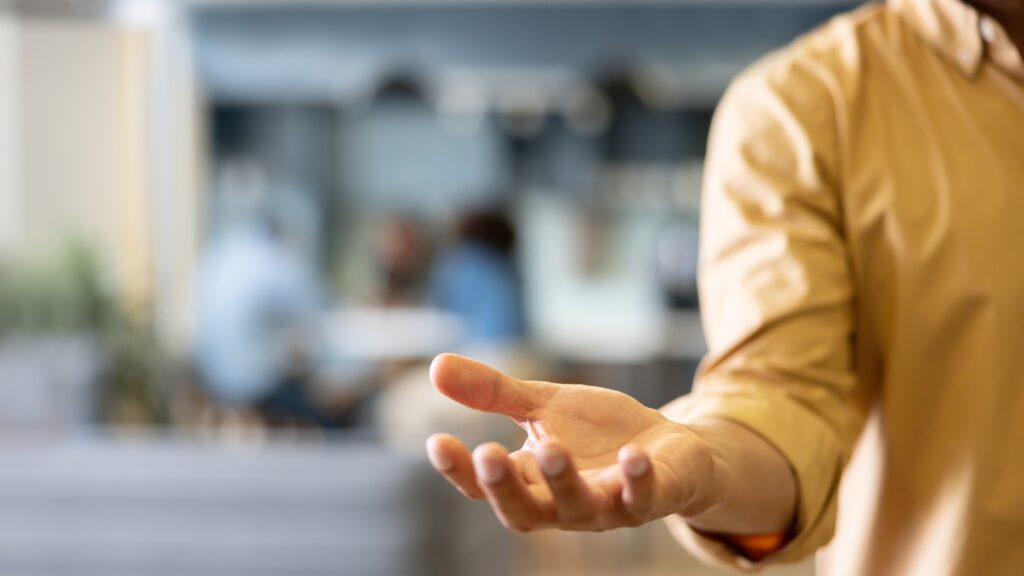 A man holds out his hand as if expecting someone to put something in it.
