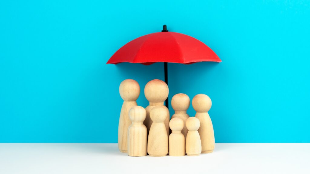 A red umbrella over a family of wooden figures against a blue background.