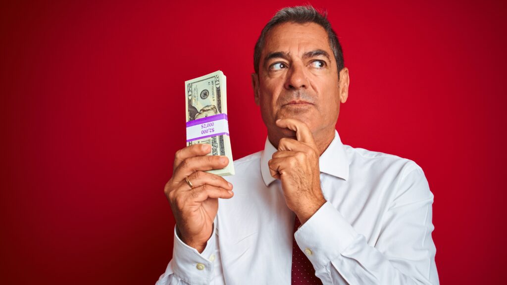 A man looking thoughtful holds a strap of cash.