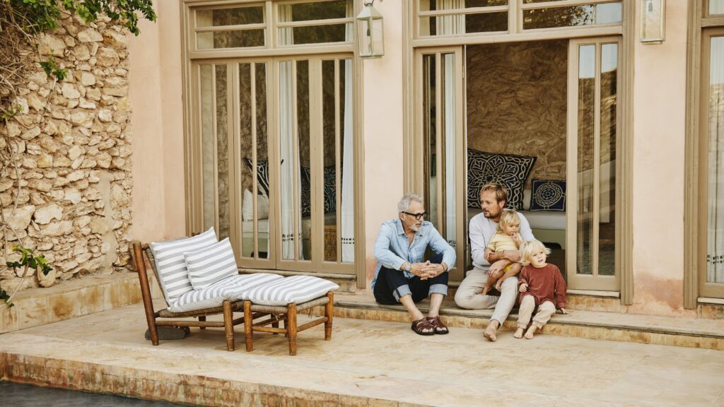 A father and adult son have a discussion while relaxing with family on a terrace.