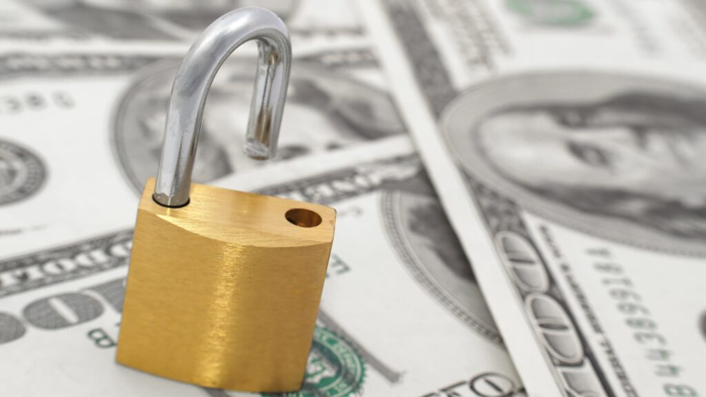 An open padlock sits atop scattered hundred-dollar bills.