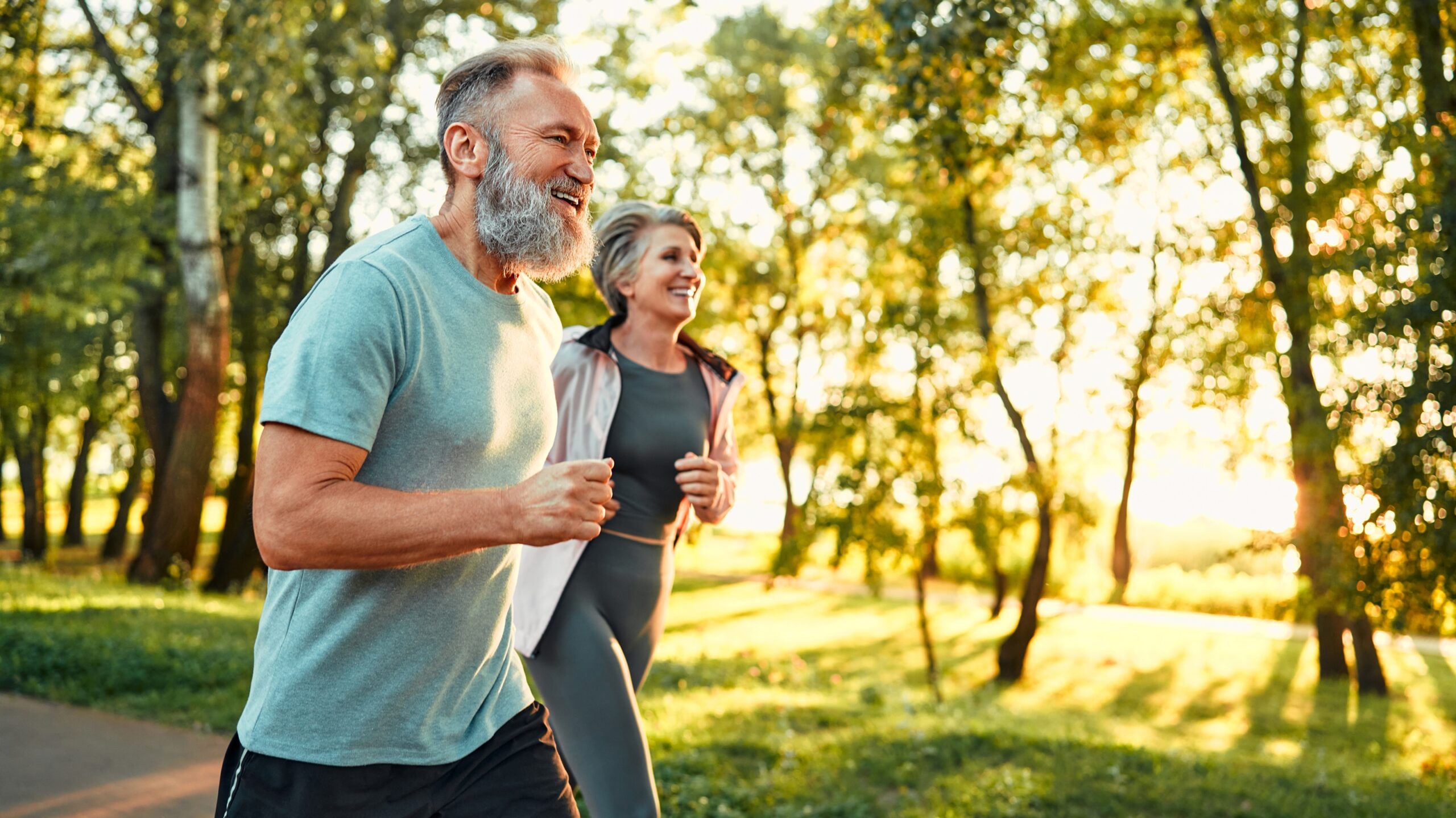 An older couple take a jog together on a park path.