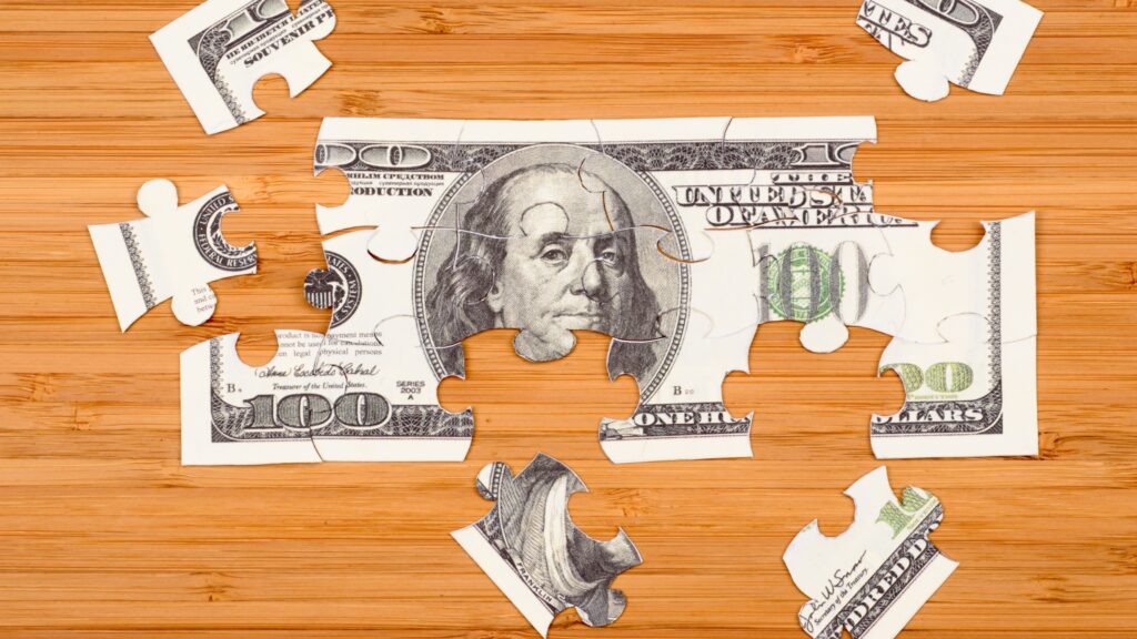 Puzzle of a hundred-dollar bill on a wooden background.