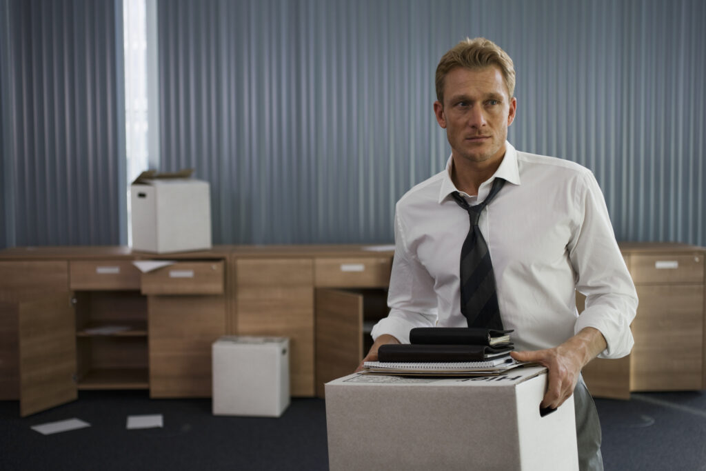 Laid off businessman moving out of office. He looks stressed but not downtrodden as he holds a box of his belongings.