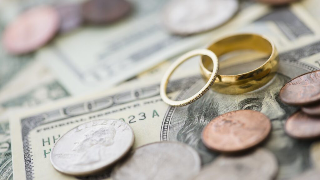 Coins scattered around wedding rings sitting on top of cash.