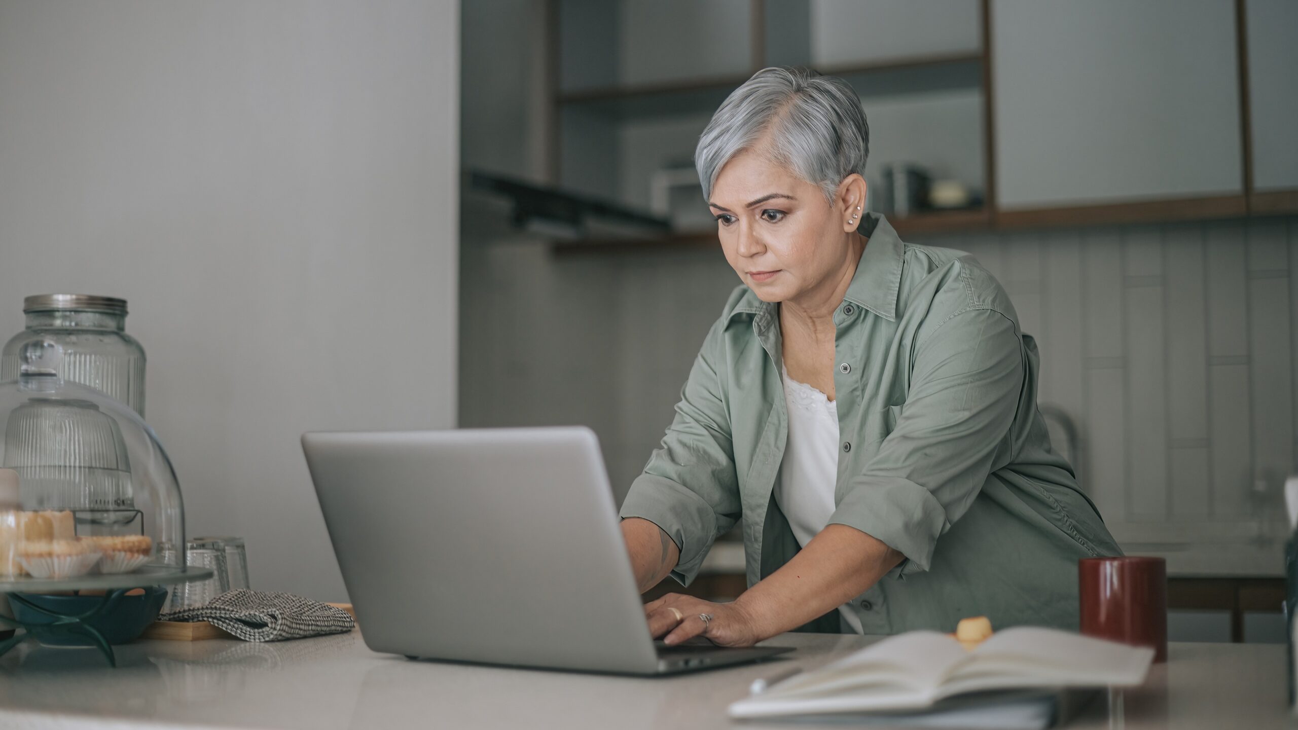 An older woman works on her laptop at her kitchen table.