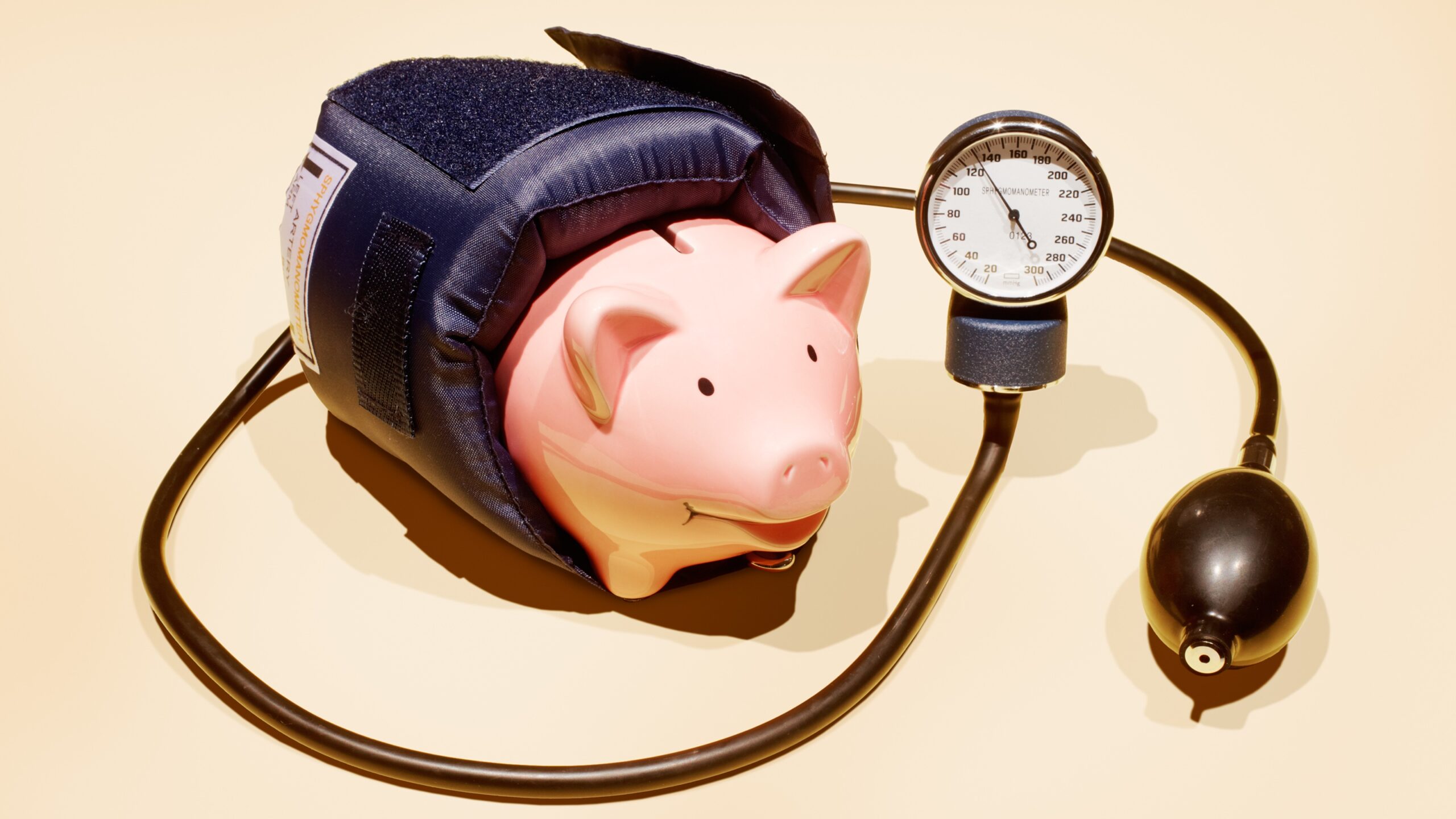 A blood pressure cuff is wrapped around a piggy bank.