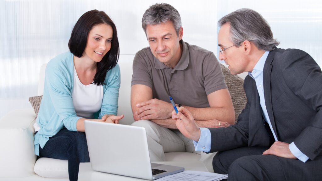 A couple talk with an adviser while sitting on their sofa and looking at a laptop.