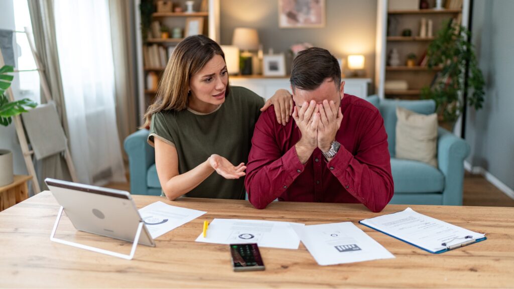 A couple look regretful as they sit at their dining room table and look at financial paperwork.