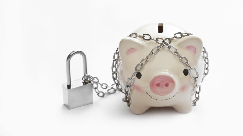 A piggy bank is wrapped in a chain next to a padlock.