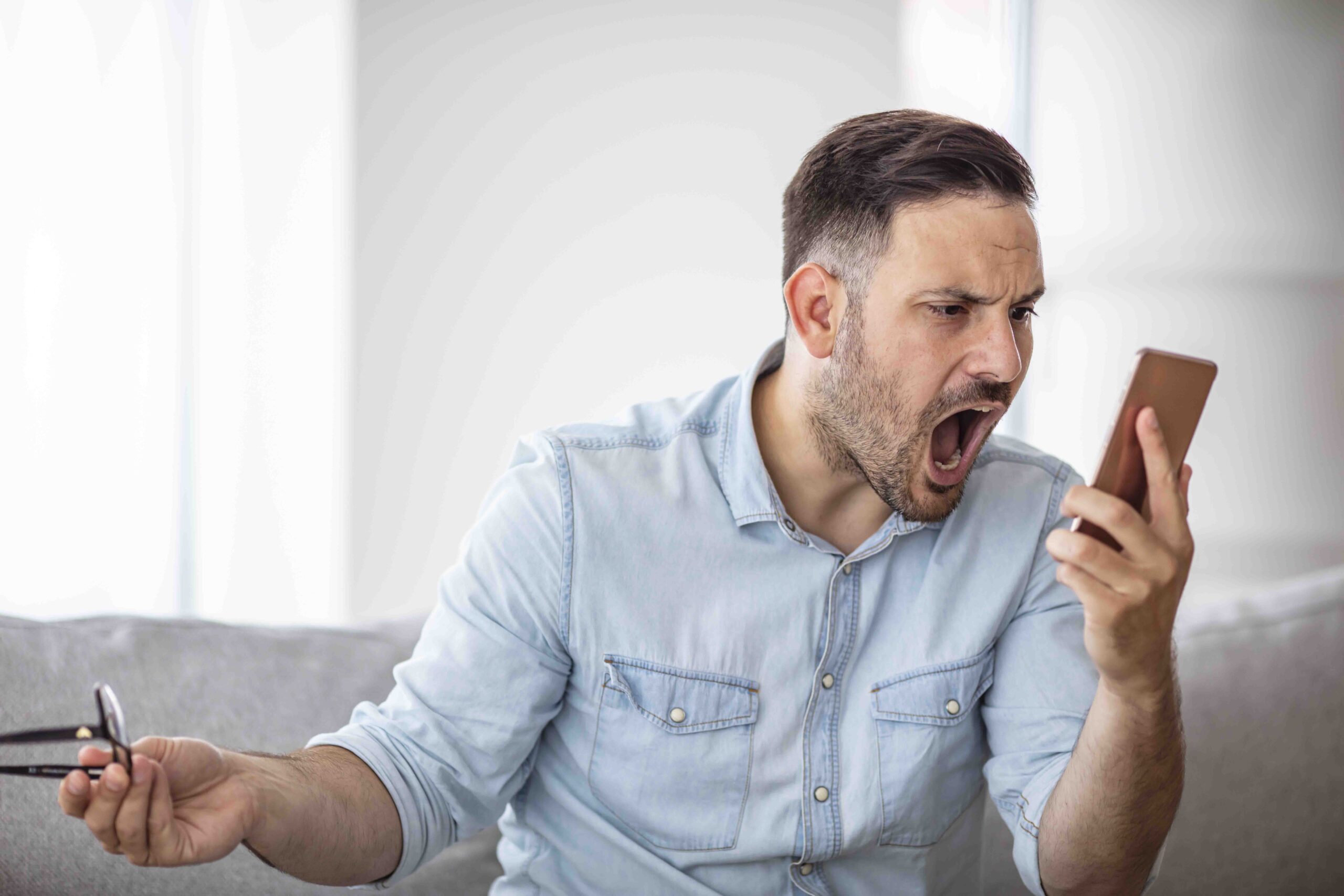 A young guy, shouting at his smartphone. Image of young furious businessman on the phone shouting. Portrait of angry young man screaming on his mobile phone
