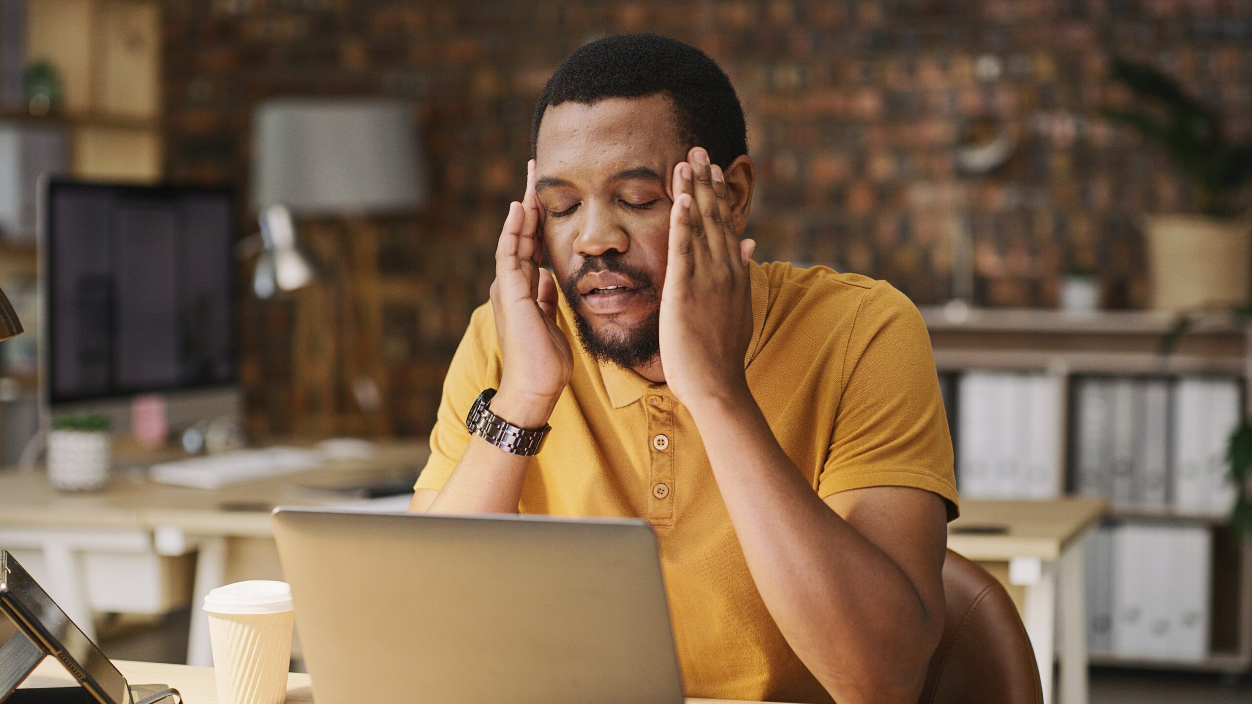 A man massages his temples as if he has a headache while looking at his laptop.