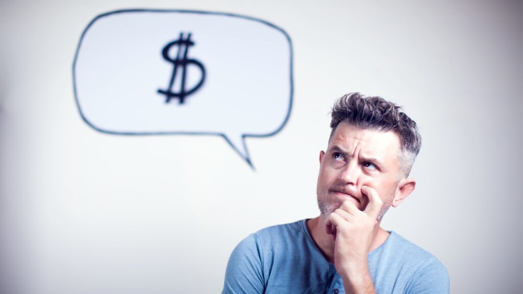 A man appears to be thinking and has a thought bubble above of his head with a dollar sign in it.