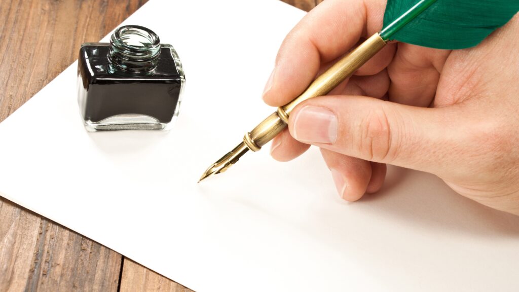 A man's hand grips a fountain pen, preparing to write on a piece of paper.