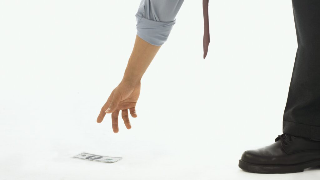 A businessman reaches for cash lying on the ground.