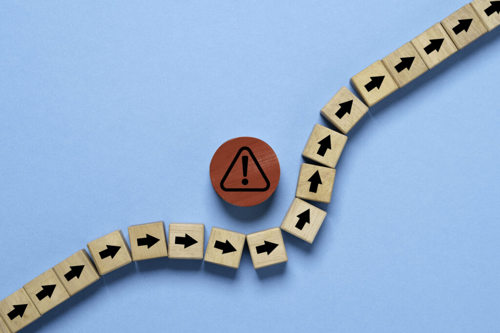 red circle block with red exclamation warning sign in the middle of a line of wooden blocks with black arrows