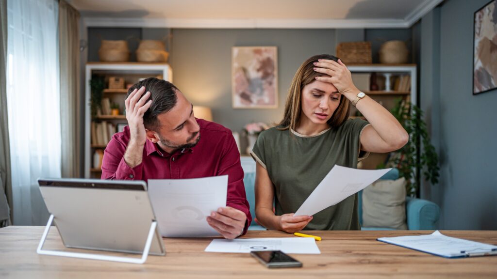 A couple look stressed over finances while looking at paperwork at their dining room table.