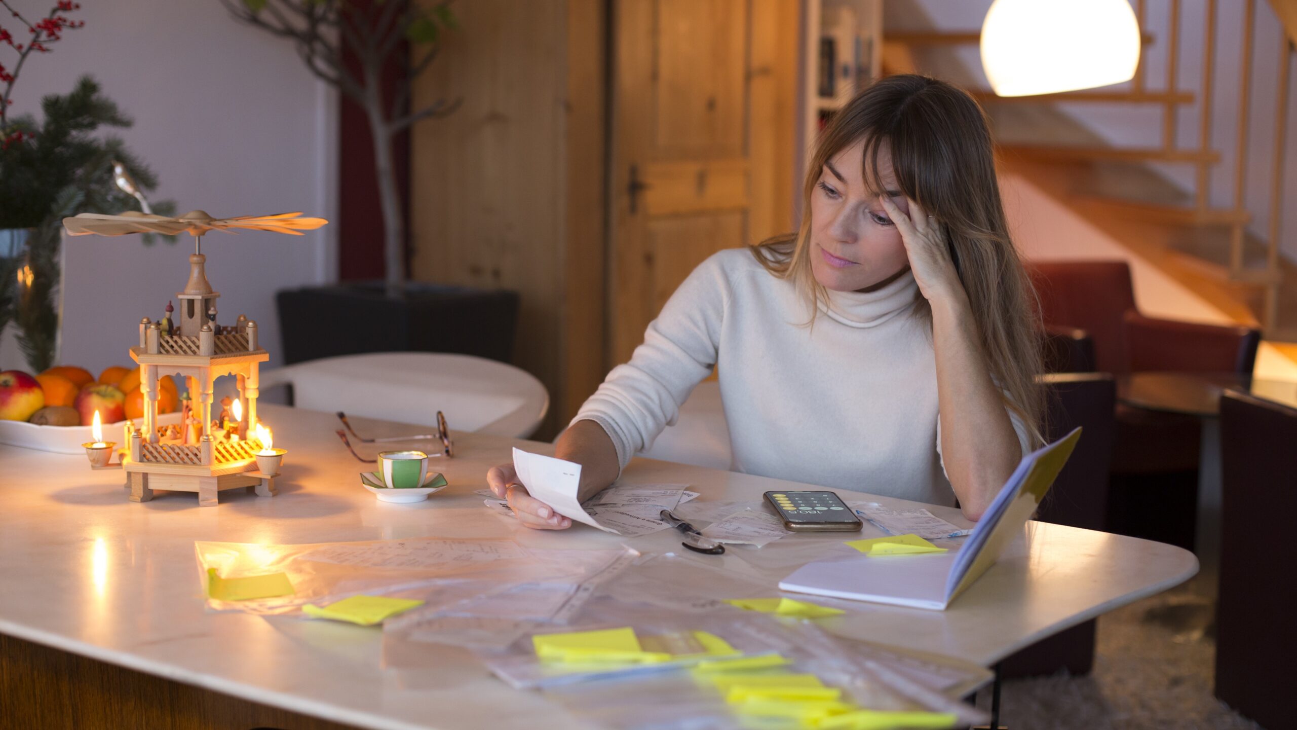 A woman looks a bit stressed while working on financial paperwork at her kitchen table.