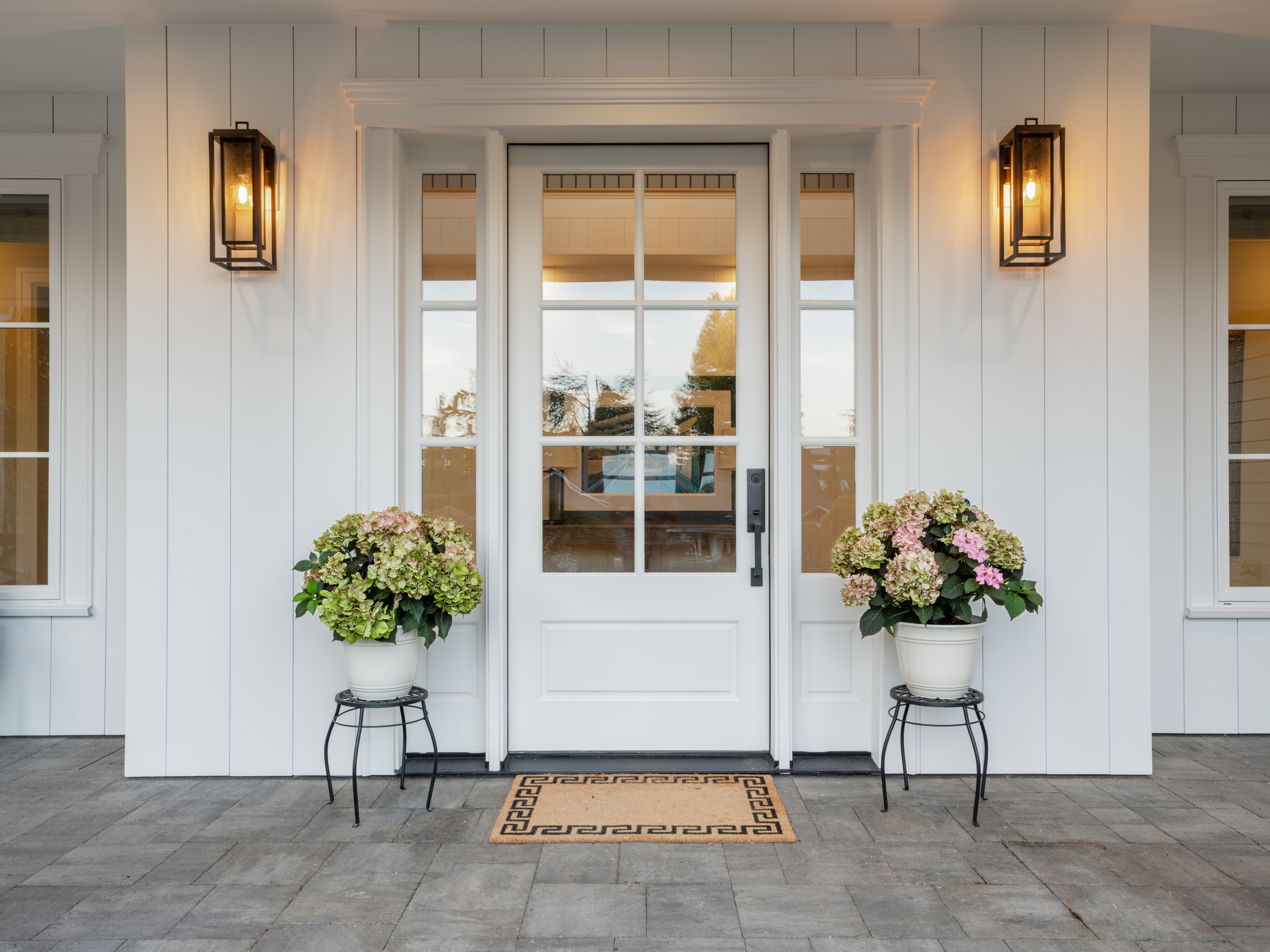 front porch of a house flanked by potted flowers and porch lights