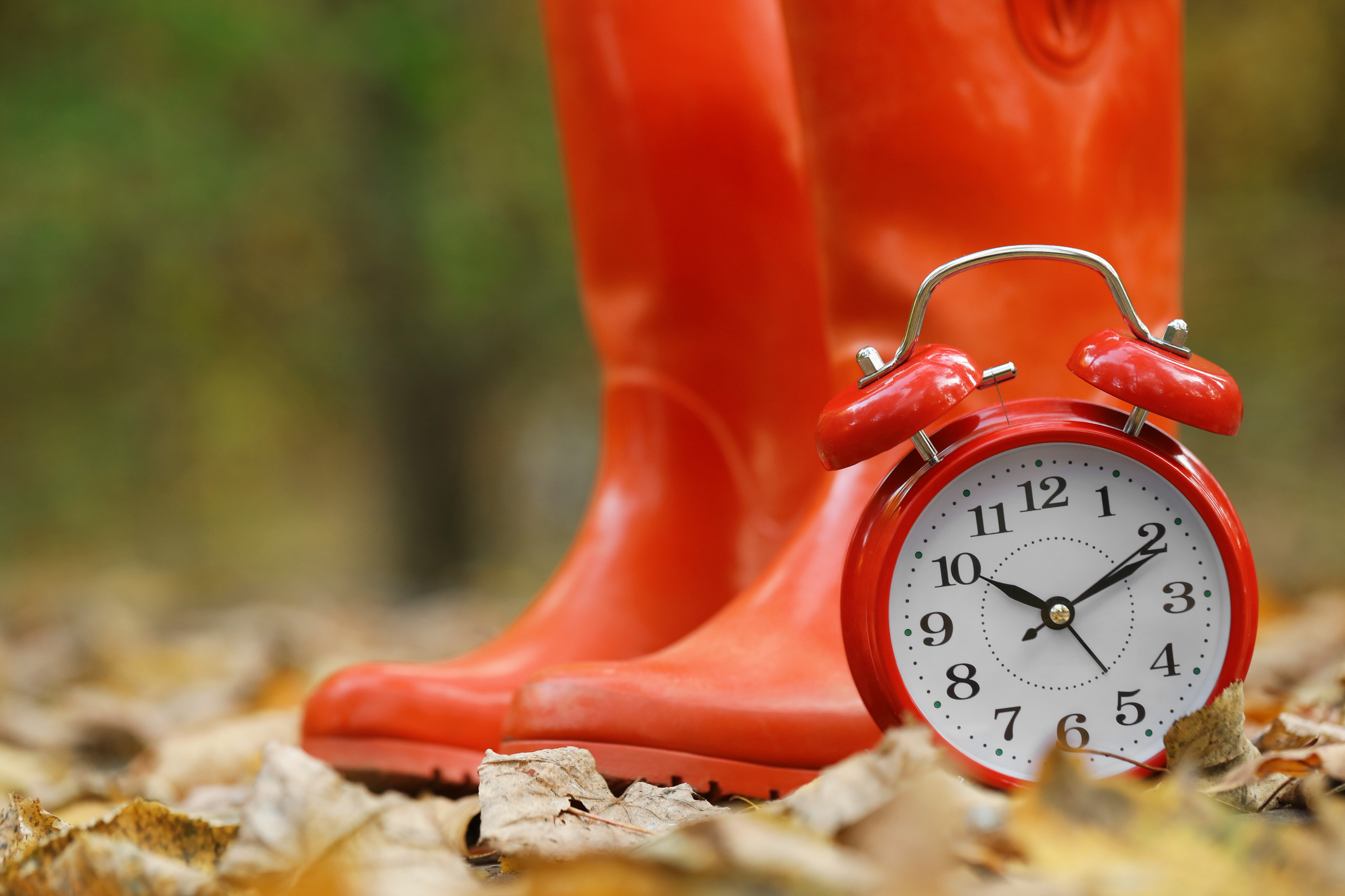 red alarm clock with red rubber boots in the background on an autumn day
