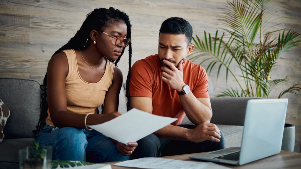 A couple look over financial paperwork on the sofa together.