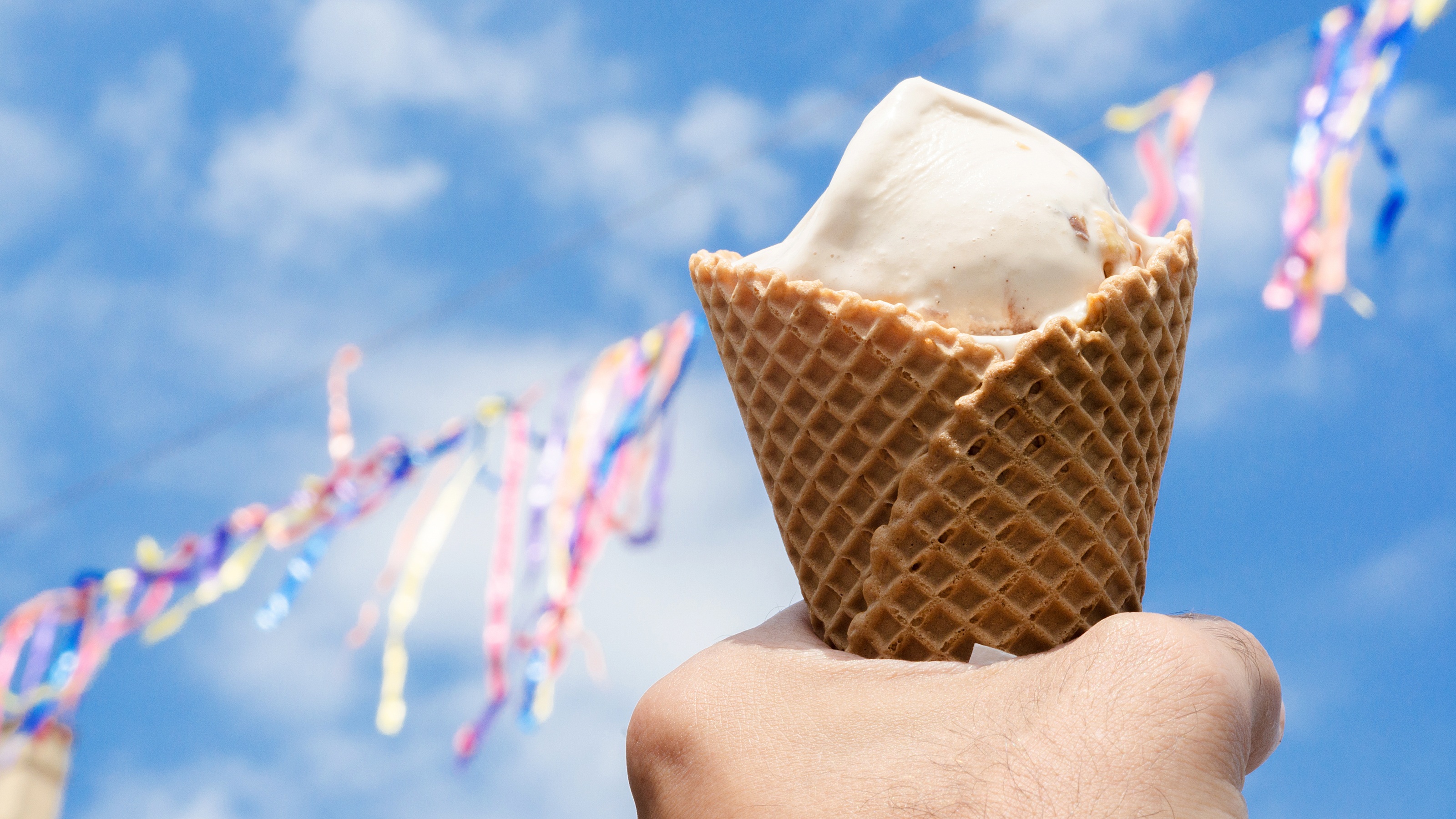 Une main tient un cornet de crème glacée. Streamers en arrière-plan.
