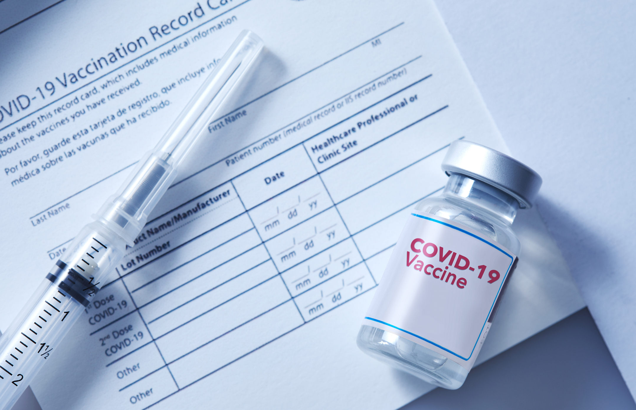 A vial of coronavirus vaccine on a vaccination record card with a syringe on the side