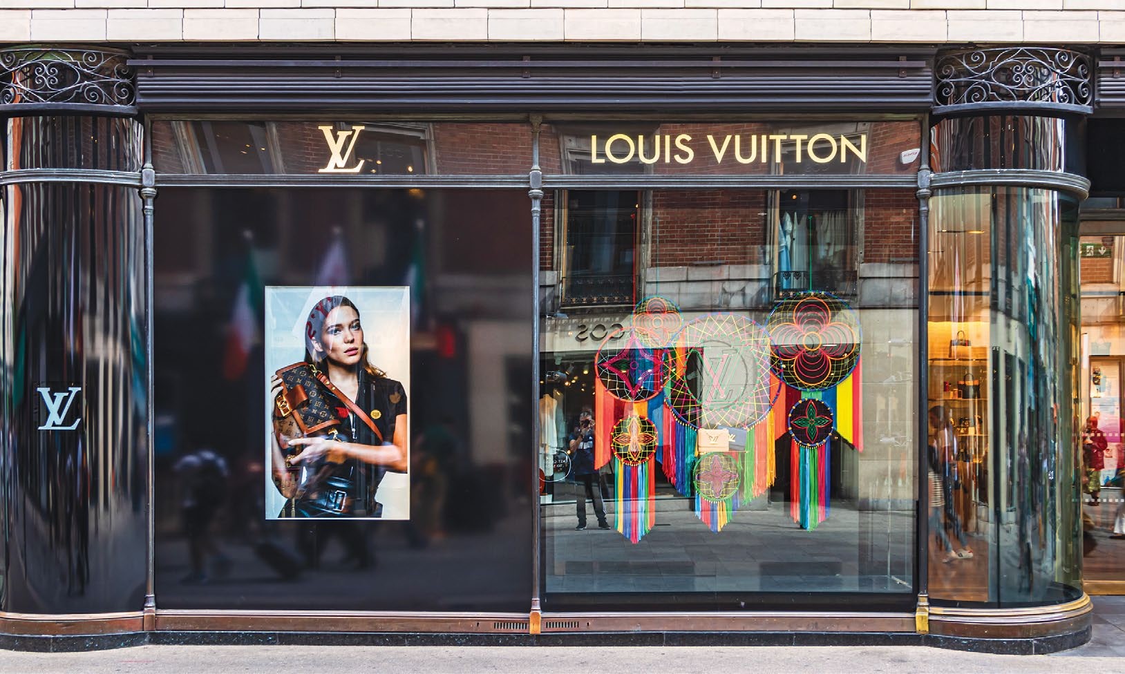 Une devanture de Louis Vuitton avec un grand portrait d'un modèle et des décorations colorées de Dreamcatcher, reflétant le luxe et le style.
