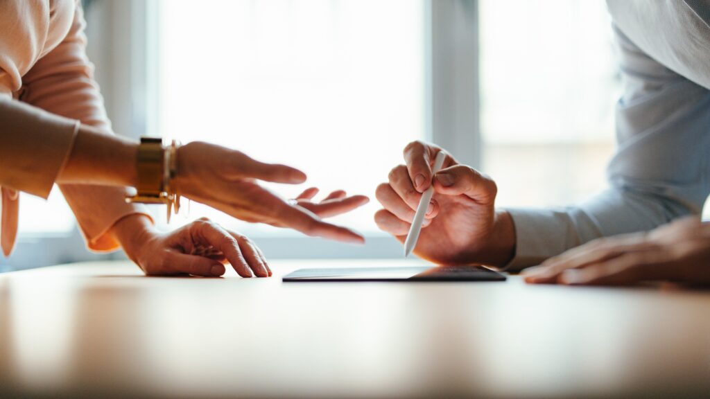 A divorcing couple negotiate, only their hands and a tablet showing.