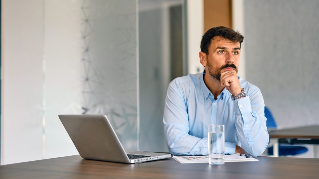 A man sits at his desk and appears to be thinking about a problem.
