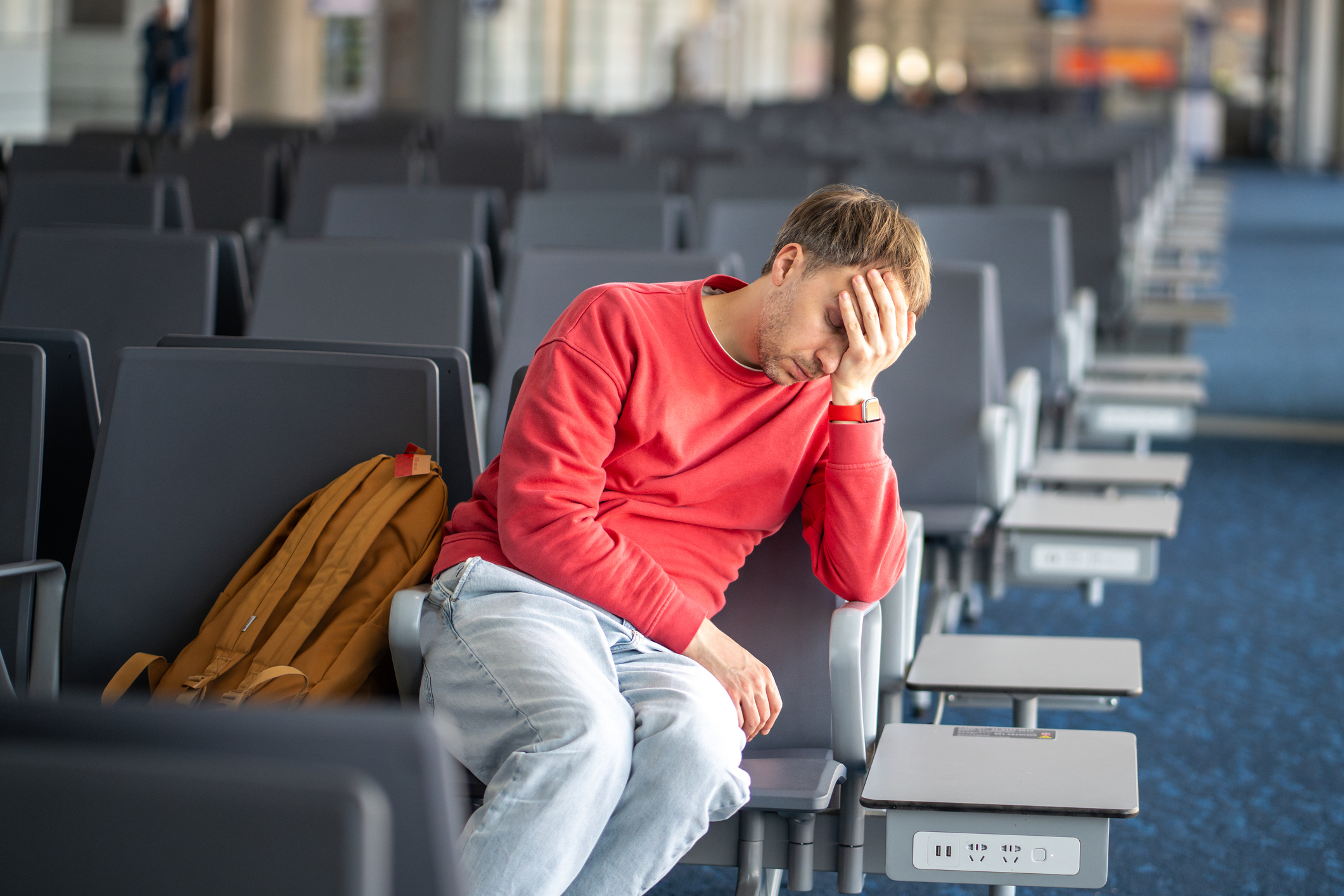 Un homme endormi fatigué s'effondre contre une chaise dans la zone d'attente de l'aéroport. Longue escale qui s'éternise, épuisement dû à l'attente, vol retardé, somnolence accablante, moral déprimé à cause du temps interminable à l'aéroport