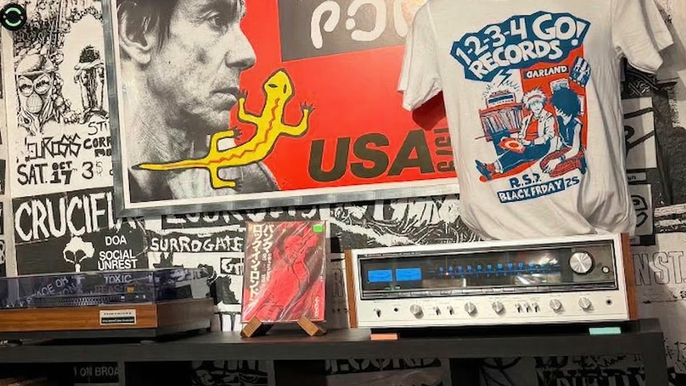 Une chaîne stéréo vintage et une platine vinyle occupent une place de choix sur une étagère, flanquées d'affiches punk et de souvenirs. L'image d'Iggy Pop a été légèrement modifiée par Gemini.