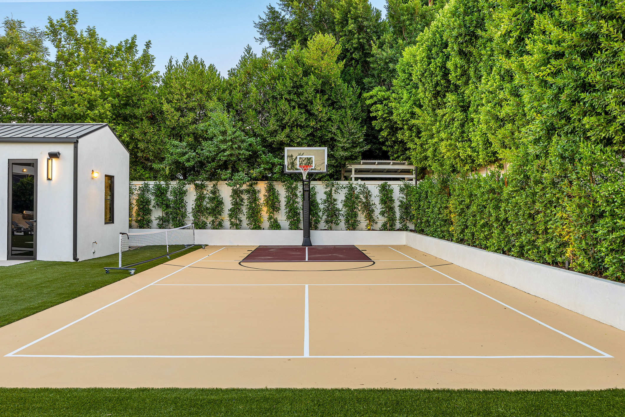 Terrain de sport moderne avec panier de basket et filet de tennis entouré d'une verdure luxuriante.