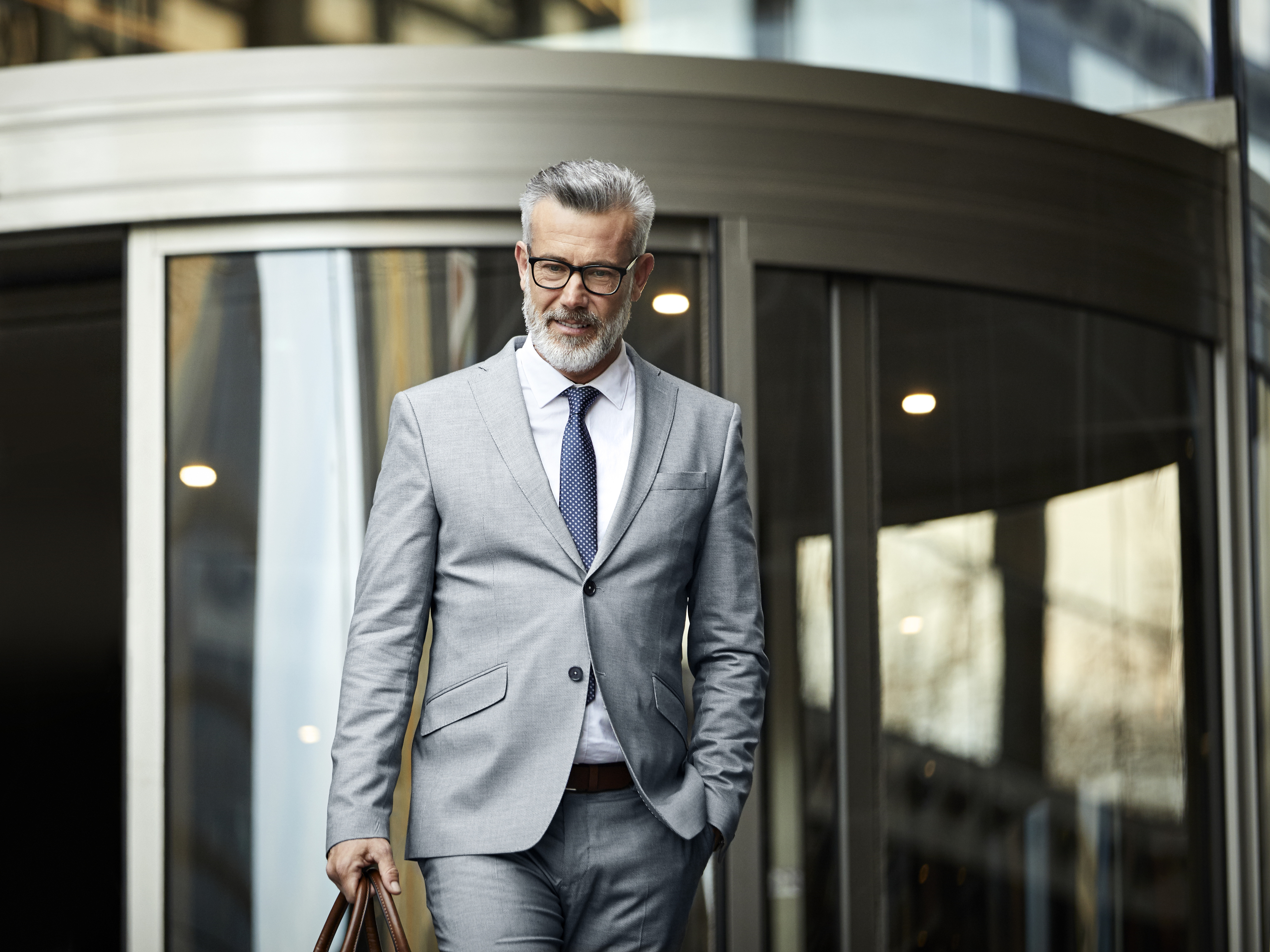 Homme d'affaires mature quittant un immeuble de bureaux. Des professionnels masculins confiants marchent hors du lieu de travail après le travail. Il porte un costume.