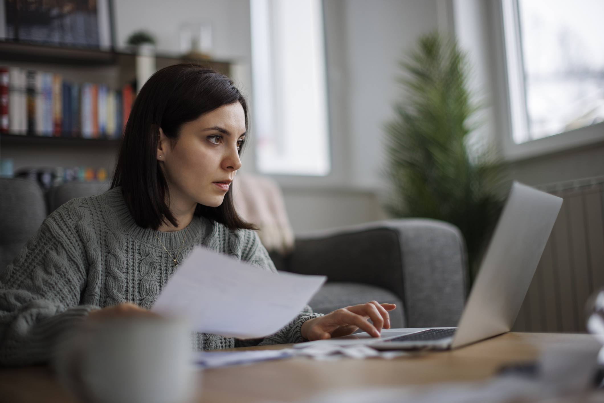 Femme vérifiant la paperasse sur un ordinateur portable à la maison