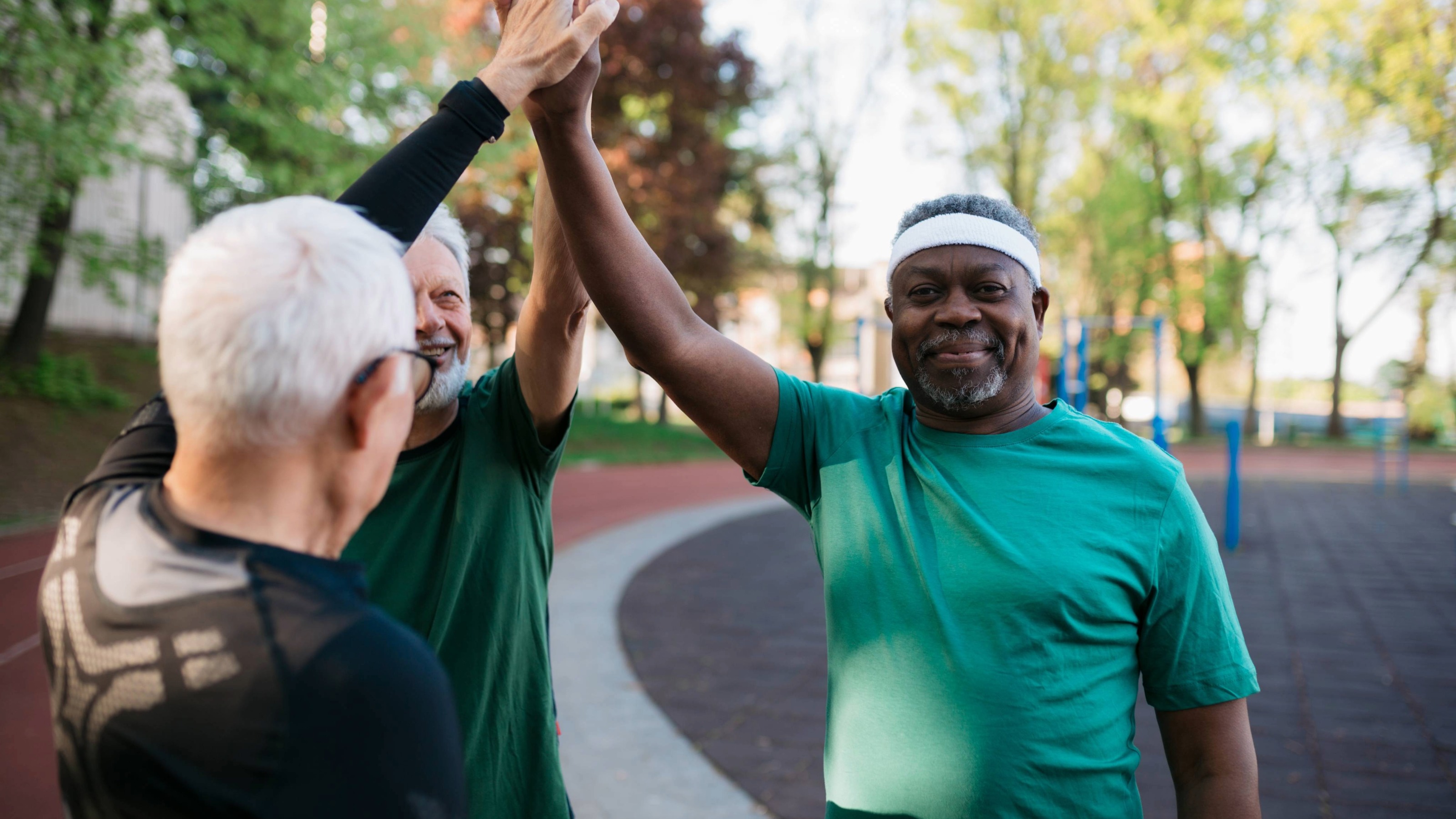 Groupe multiracial d'hommes âgés se donnant un high five après une séance d'entraînement sur un terrain d'exercice.