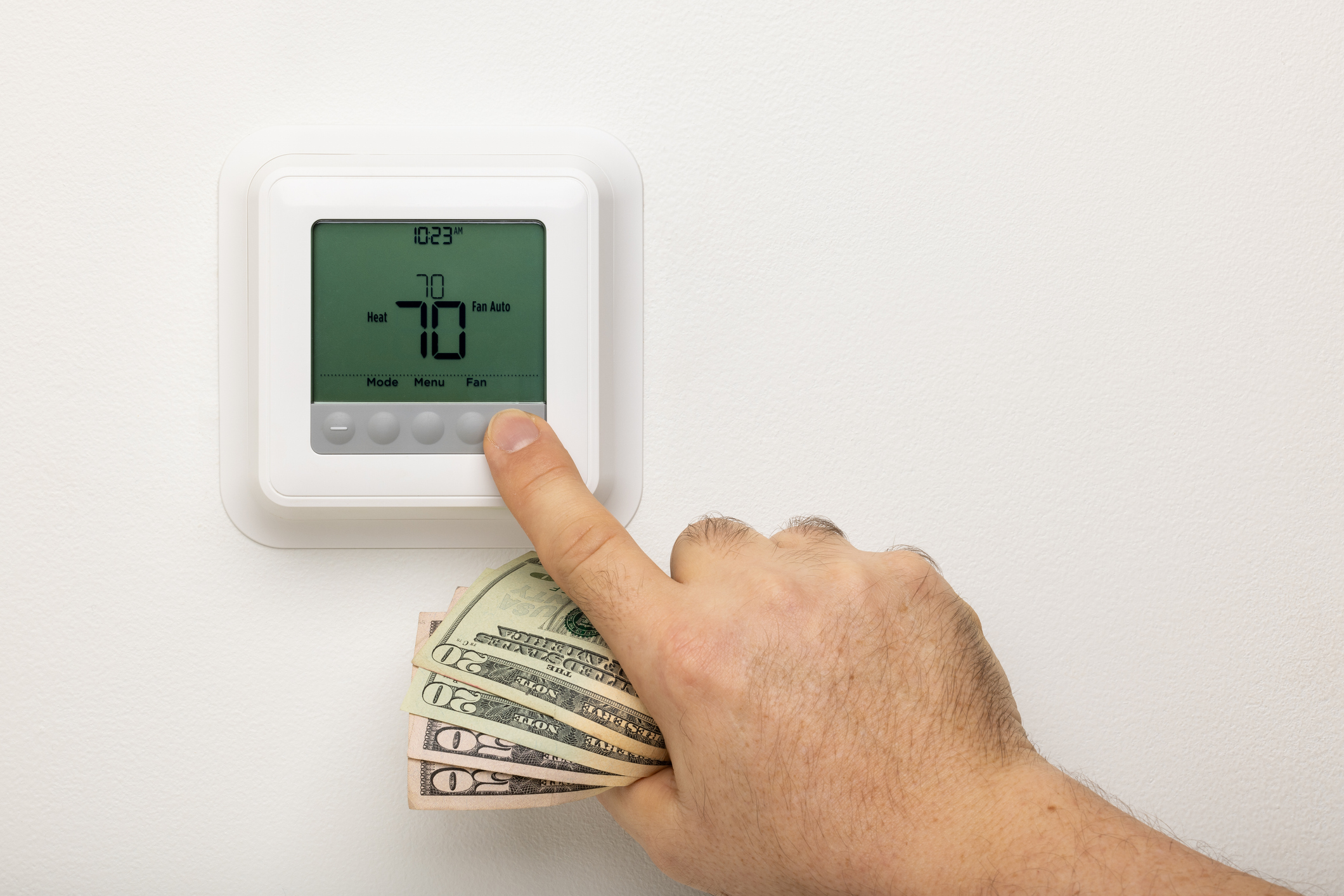 Une main tenant de l'argent ajustant un thermostat sur un mur.