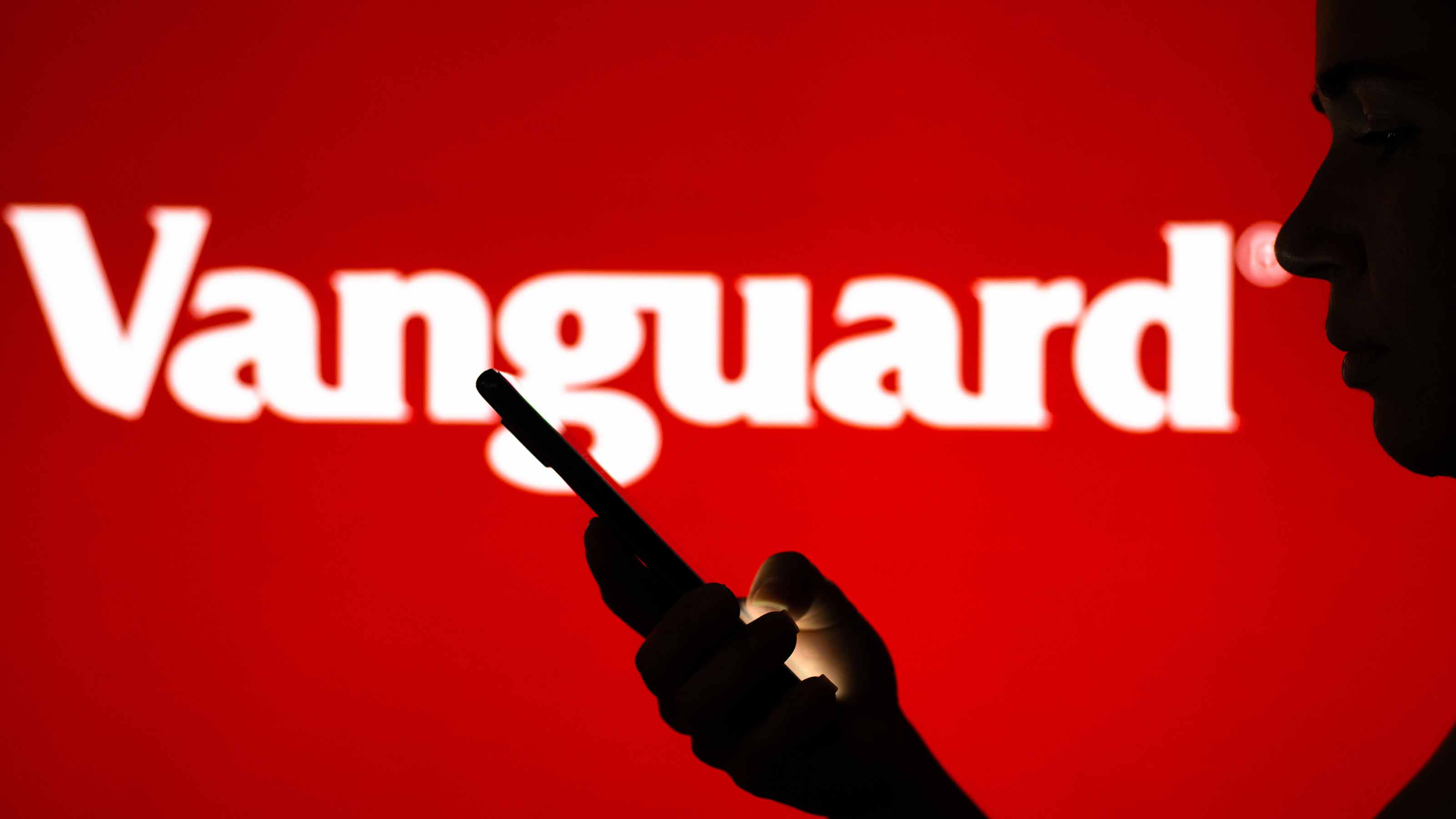 Logo Vanguard sur écran rouge avec une personne regardant un smartphone